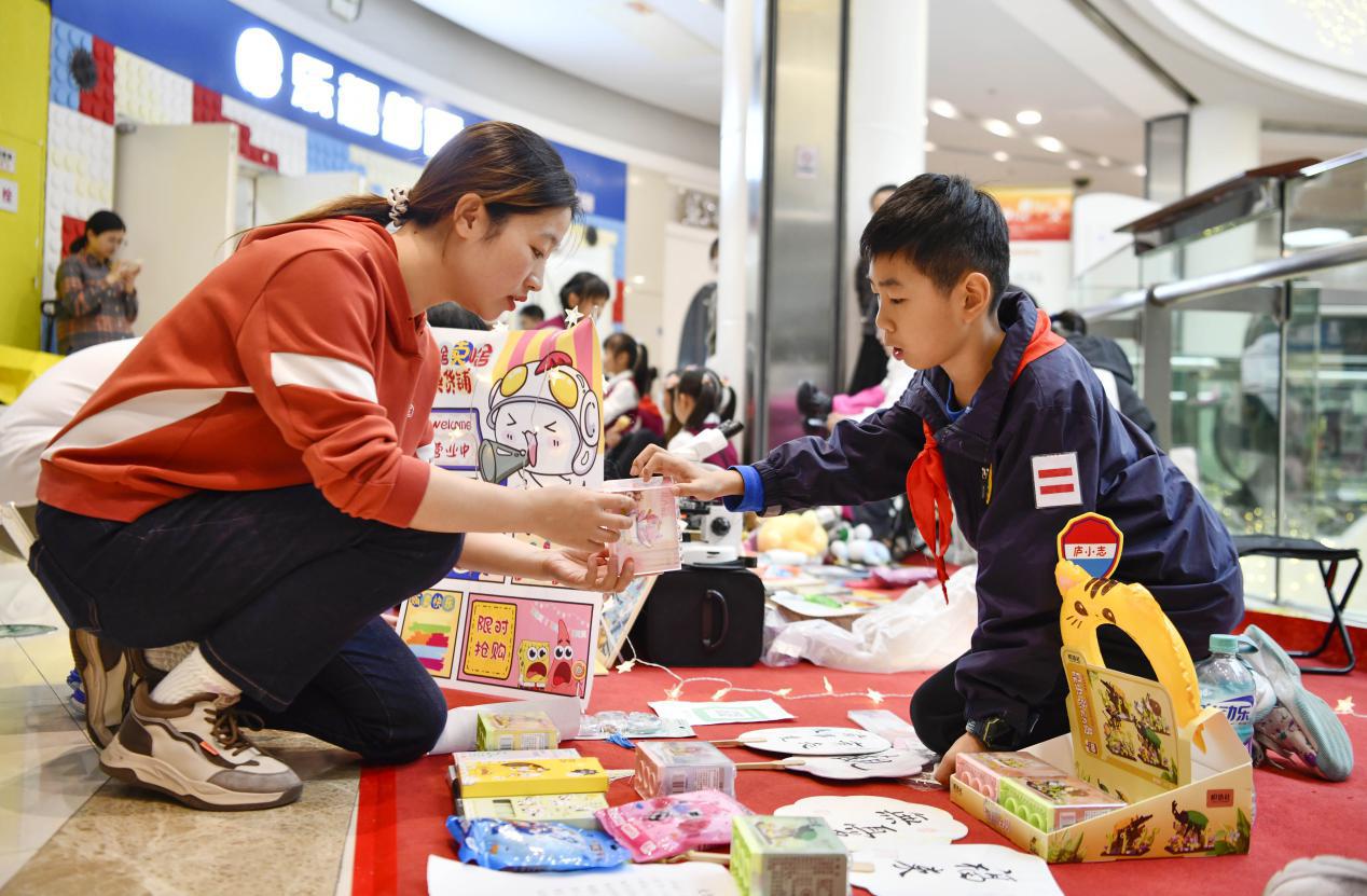 图1：2024年10月19日，安徽合肥，在安徽省合肥市庐阳区一家大型商场内，小志愿者在摊位上义卖物品。